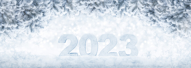 New Year card with ice number 2023 on snow. Snow covered spruce branches with Christmas blurred garland lights on the banner. Beautiful, winter, holiday background with a copy space.