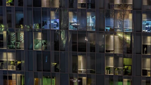 Night aerial view of office building glass panoramic window facade with illuminated lighted workspace rooms timelapse. Glowing light in skyscraper