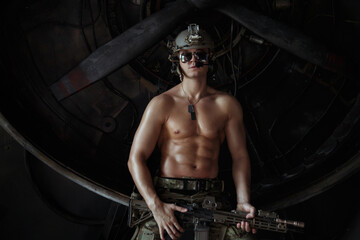Fototapeta na wymiar A strong attractive soldier with a muscular torso in an American camouflage uniform with a submachine gun in his hand.