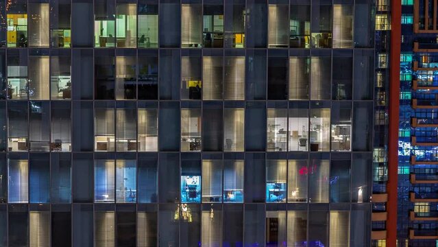 Night aerial view of office building glass window facade with illuminated lighted workspace rooms timelapse. Glowing and flashing light in skyscraper