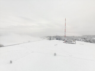 Aerial photo of radio and TV mast in front of wall of fog in snow on hillside