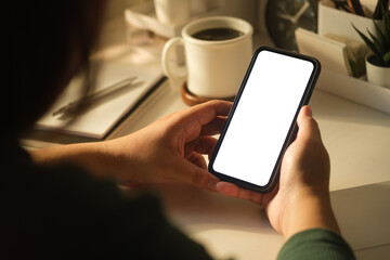 Woman hands holding mobile phone while sitting at her workplace. White empty screen for your advertise design.