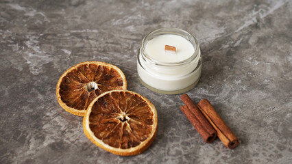 Fototapeta na wymiar Handmade candle with wooden wick in white glass jar with cinnamon and dry oranges at the background, winter cozy home decoration