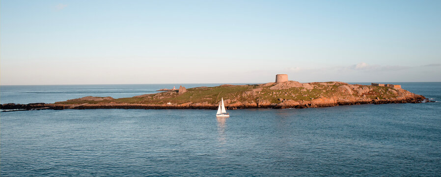 Dalkey, Ireland - Nov 5, 2022: View of Dalkey island and Saint Begnets Church ruins with a white yacht sailing by just before sunset