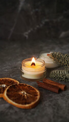 Aromatherapy. Candle in a glass with slices of orange, cinnamon sticks and fir branches. Modern homemade candle with wooden wick. Vertical photo