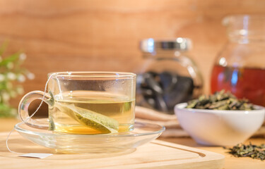 Front view, glasses cup of hot herbal tea with lemon, teapot, dried tea leaves in background.