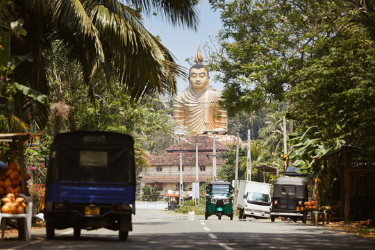 Traffic on rural road against Buddha statue. Wewurukannala Buduraja Maha Viharaya Buddhist temple in Dikwella, Sri Lanka..