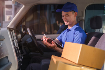 Smiling delivery man with packages sitting in driver seat of van and reading addresses on digital tablet.