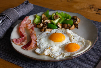 Two fried eggs with bacon, green peppers and mushrooms. Traditional English breakfast concept