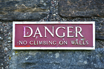 Close Up of Metal Sign on Stone Wall 'Danger No Climbing on Walls' 