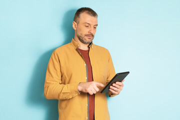 Modern technologies. Confident middle aged man holding and using digital tablet, standing over blue studio background