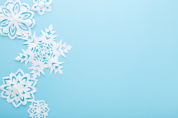 Different white snowflake shapes created from paper on light blue table background. Pastel color. Closeup. Top down view. Handmade decoration elements for winter festive. Empty place for text.