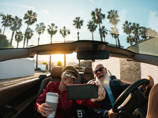 Senior couple having fun doing selfie inside a convertible car during holiday vacation - Elderly...
