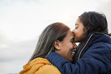 Latin child kissing her mother outdoor during winter time - Focus on mom face - Mother day concept