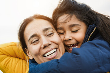 Happy latin mother and daughter having fun together outdoor during winter time - Focus on girl face