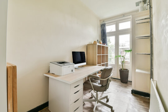 A Room With A Desk, Chair And Computer On The Wall Next To It Is A Window That Looks Out Onto An Outside View