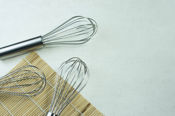 whisk placed on Thin white on a wooden stand. On the background is uneven white plaster