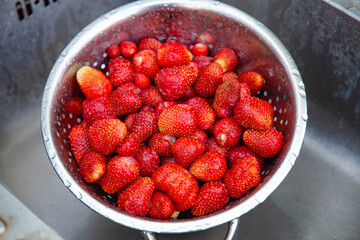Freshly picked bright strawberries are washed in a metal colander in a old sink.