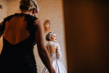 Bridesmaid helps a beautiful smiling blonde bride in the morning with preparations. Wedding, photography.
