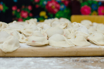Traditional homemade food. Slavic traditional dish. Dough for dumplings. Raw meat dumplings on a wooden board. The process of making dumplings.