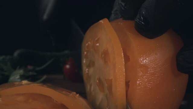Chef cutting fresh yellow tomato with a knife on wooden cutting board at restrain kitchen, macro close-up. Preparing to cooking salad. Slow motion 