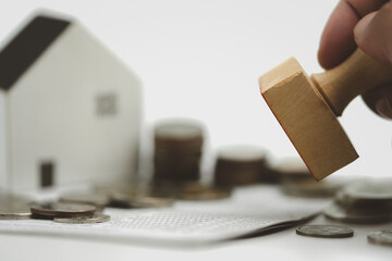 Close up wood stamp in hand with home and coin, concerning mortgage loan offer for and house...