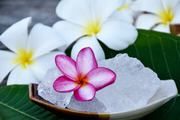 Soft focus of purple plumeria flower and white alum cube on ceramic pot and white plumeria flowers background, spa and skincare concept.
