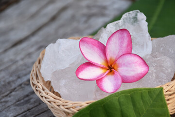 Soft focus of purple plumeria flower and white alum cube on wicker basket, spa and skincare concept.