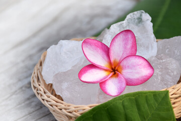 Soft focus of purple plumeria flower and white alum cube on wicker basket, spa and skincare concept.