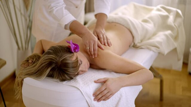 Woman with flower in hair enjoying spa center while getting relaxing massage.