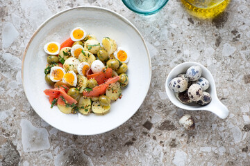 Plate with potato, smoked trout and quail eggs salad, flat lay on a light-brown granite background, horizontal shot