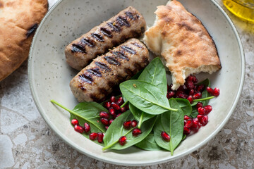 Beige plate with grilled kabobs, spinach and pomegranate salad, flatbread, middle closeup, horizontal shot