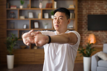 Mature asian man stretching hands, working out at home in living room interior, copy space