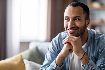 Smiling Handsome Black Guy Sitting On Sofa At Home And Looking Away