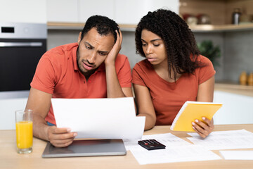 Despaired millennial black family in red t-shirts work with documents, check bills, have problems