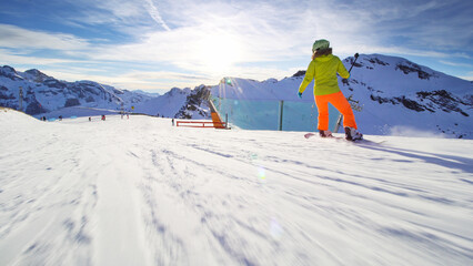 Girl snowboarding on slopes in the Swiss alps. Sun rays and flare visible.
