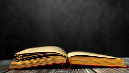Image of an open antique book on a wooden table with old yellow sheets and dust on a dark background. Side view.