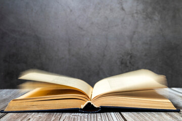 Image of an open antique book on a wooden table with old yellow sheets and dust on a dark background. Side view.