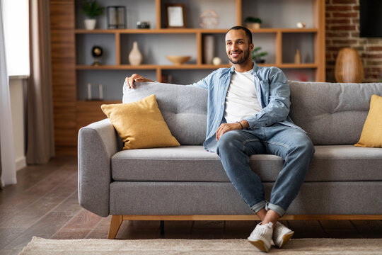Domestic Comfort. Smiling Young Black Man Resting On Sofa In Living Room