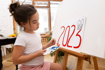 A girl draws 2023 with red bunny ears. Symbol of happy Chinese 2023 New Year.