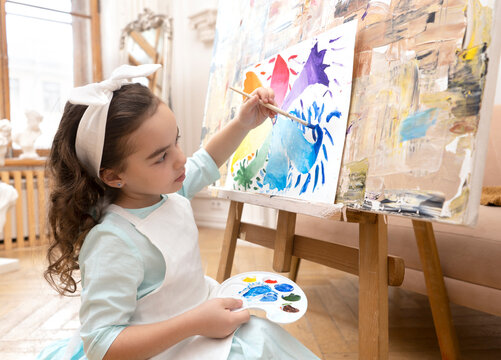 Cute girl drawing with a paint palette and a paintbrush. Little painting artist.