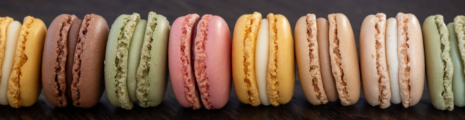 sweet and colorful french macarons lined up on dark wooden table , gluten free dessert. panorama