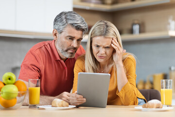 Anxious couple having healthy breakfast, using digital tablet, experiencing difficulties