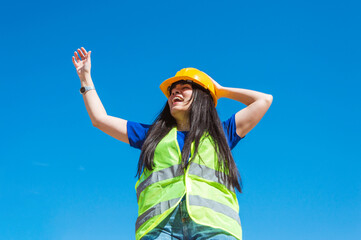 woman with engineering helmet and safety vest is outdoors laughing content with open arms