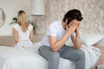 Relationship crisis. Caucasian man feeling upset after fight with his wife, sitting back to back on bed at home - obrazy, fototapety, plakaty