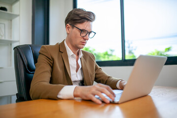 Portrait of handsome businessman working at the office with laptop, using computer on table.