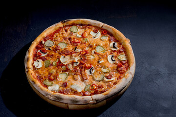 Appetizing pizza with hunting sausages, mozzarella cheese, pickled cucumbers, chili peppers on a tomato base on black background