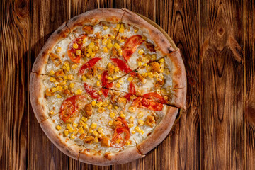 Pizza for children on a cream base with chicken fillet, tomatoes, corn and mozzarella cheese on wood background