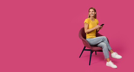 Cheerful adult caucasian female blonde in casual sitting on chair, chatting on smartphone