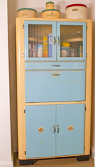 Antique 1950's kitchen larder cabinet in pale blue and cream. Multiple drawers and doors with frosted glass fronts. Classical genuine kitchen cabinet. Old cake and biscuit tins sit on top. Retro.